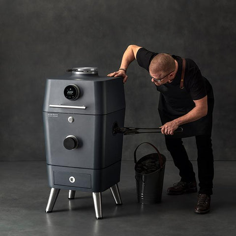 Everdure 4K Mat Zwart kamado grill met digitale display, man vult houtskool bij.
