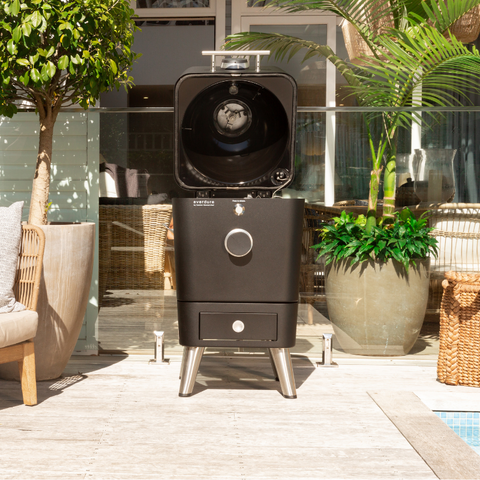 Everdure 4K Mat Zwart kamado grill met open deksel, touchscreen en RVS poten op een terras.