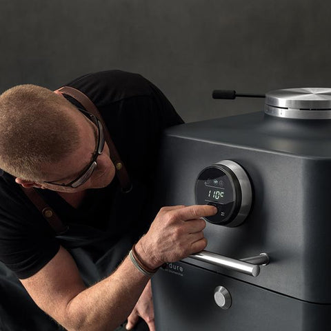 Man stelt de Everdure 4K Mintblue kamado in, met digitaal display en metalen handvat.