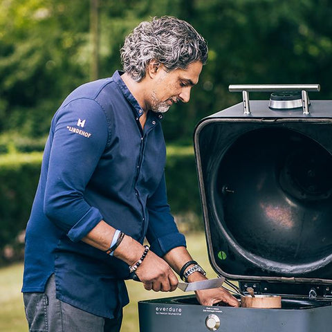 Man kookt met een Everdure 4K Mintblue kamado grill, met open deksel en houtskool.