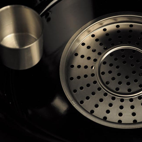 Close-up van de roestvrijstalen geperforeerde grillplaat en een metalen beker in een zwarte Everdure 4K kamado.