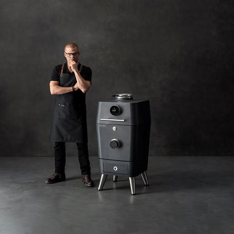 Heston Blumenthal naast de Everdure 4K White model 2026, een moderne donkergrijze kamado met touchscreen.