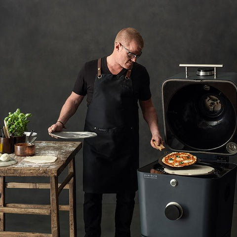 Man in zwarte schort bereidt pizza in een witte Everdure 4K kamado grill.